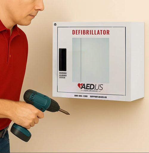 Man holds electric screwdriver in hand with the AED cabinet installed on the wall - AED.US