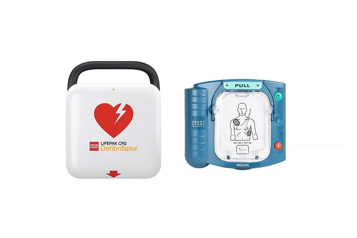 Two defibrillators, one white with a red heart symbol and the other blue with a clear panel showing a diagram, on a white background.