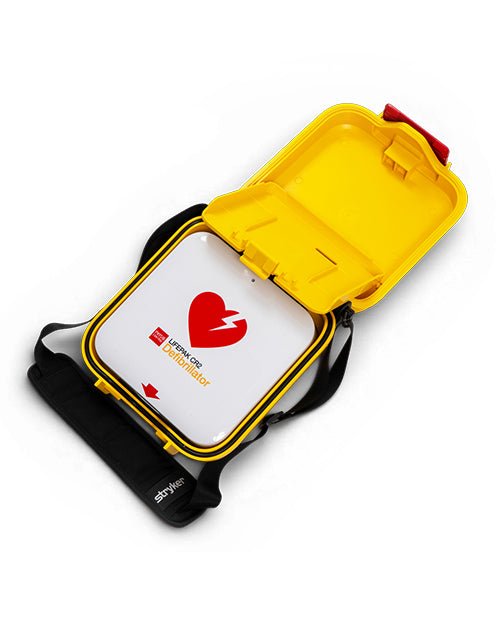 A yellow and black AED (Automated External Defibrillator) carrying case shown open, revealing a white inner panel with a red heart logo and the text 'AED User Manual'.